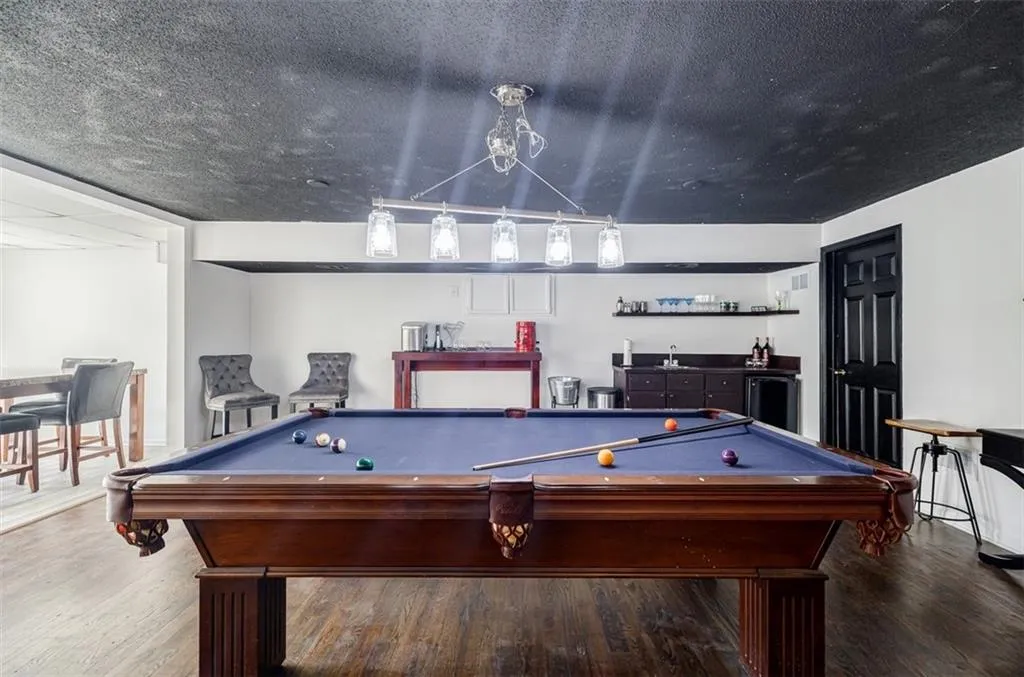 Playroom with a textured ceiling, pool table, wood finished floors, and bar area