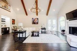 Living room featuring a notable chandelier, high vaulted ceiling, a fireplace with raised hearth, dark wood finished floors, and beamed ceiling
