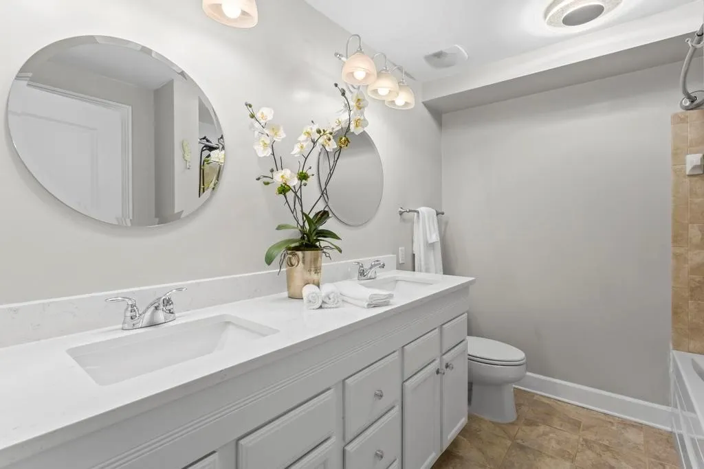 Full bathroom featuring dual sinks, new quartz countertops, tiled shower / bath combo, vanity with extensive cabinet space, toilet, and tile floors