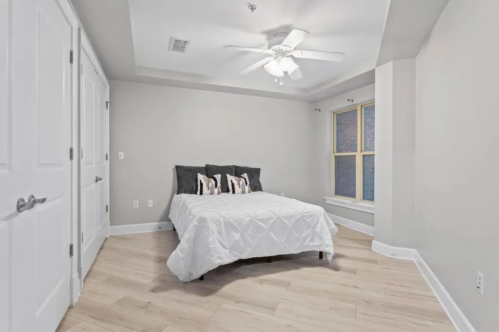 Bedroom #2 with light wide plank wood flooring, ceiling fan, and a raised ceiling