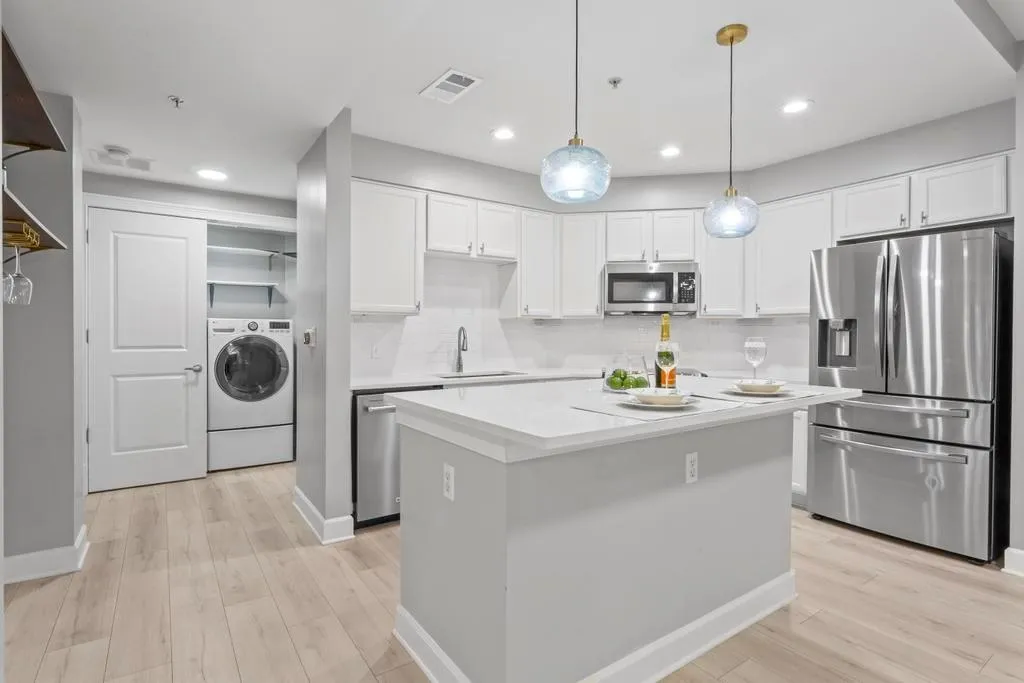 Kitchen with white cabinets, hanging light fixtures, appliances with stainless steel finishes, sink, and washer / dryer