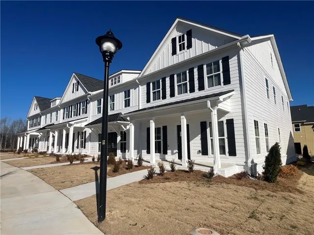 Newly constructed townhome with white siding, black shutters, and a covered porch