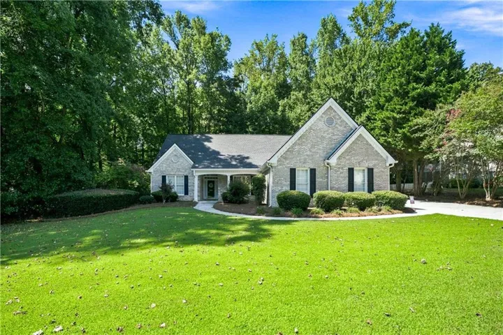 Brick facade, covered front porch, gabled roofline, black window shutters, mature landscaping