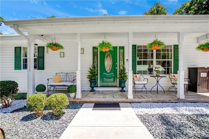 Expansive covered front porch with white columns, wood-finish flooring, and a green entry door with decorative glass
