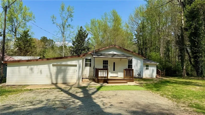 Rear view of house featuring covered porch, driveway, a garage, and a yard