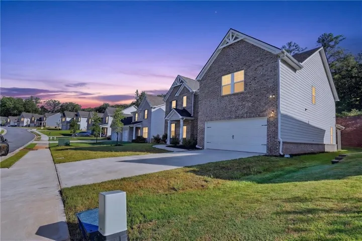 Brick and siding exterior with architectural gable detail, concrete driveway, attached garage, and landscaped lawn