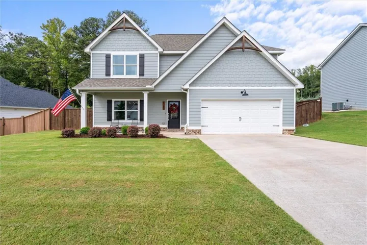 Gabled roofline with decorative wood accents, light gray siding, covered front porch, attached garage, and concrete driveway