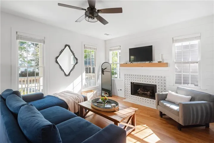 Living area with healthy amount of natural light, wood finished floors, ceiling fan, and a tiled fireplace