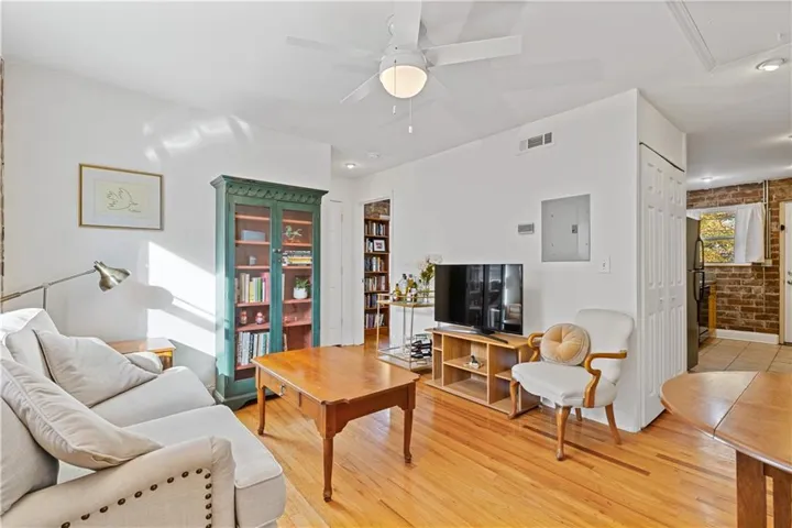 Living area featuring a ceiling fan, electric panel, brick wall, light wood-style floors, and recessed lighting