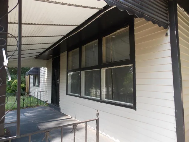 Front porch with a corrugated metal awning, white siding, and dark trim