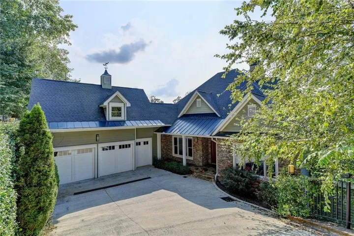Multi-gabled roofline with a cupola and weathervane, three-car garage with white paneled doors, stone and siding exterior, and a paved driveway