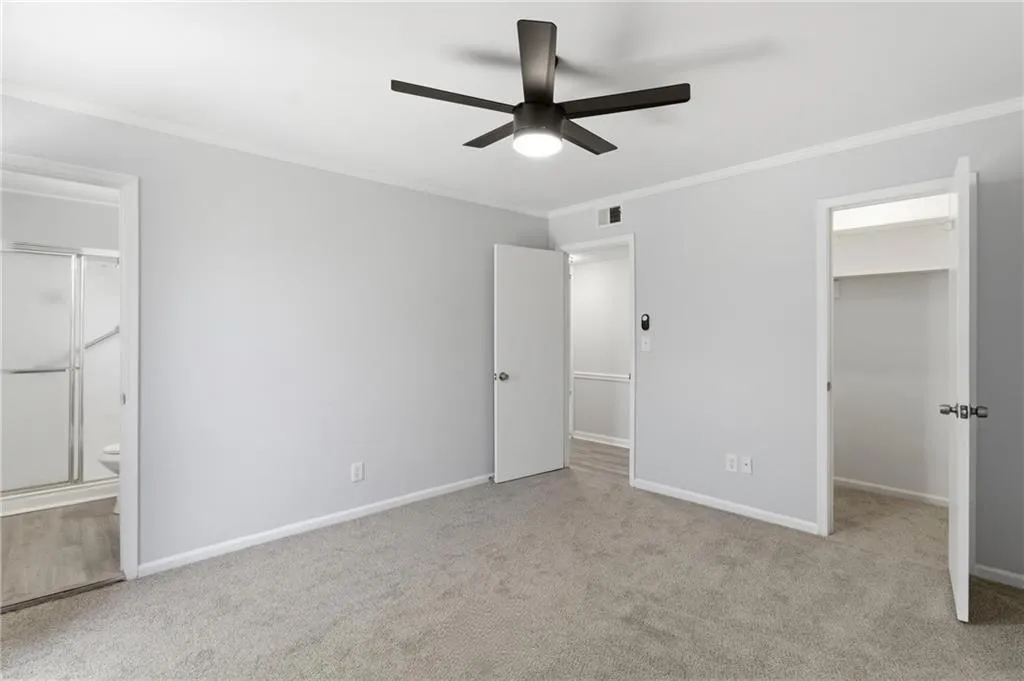 Unfurnished bedroom with ornamental molding, light colored carpet, a walk in closet, a ceiling fan, and ensuite bathroom