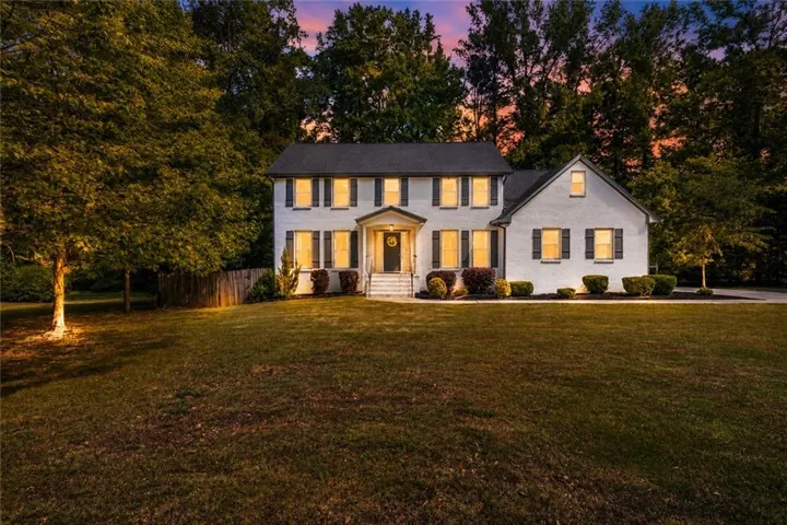 White exterior with dark shutters, covered front entry, and mature trees