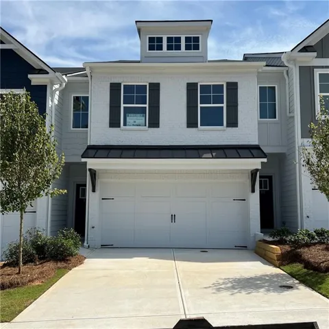Contemporary townhouse featuring a white brick and siding exterior, a two-car garage, a dormer with multiple windows, and a black metal awning