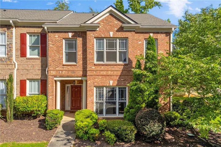 Brick townhouse exterior featuring a covered entry, white columns, a red panel door, white window frames, and mature landscaping