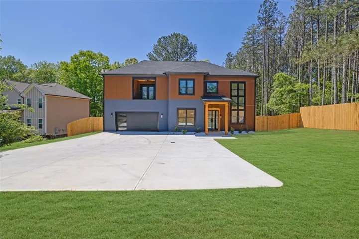 Modern exterior with an attached garage, expansive concrete driveway, natural wood fencing, and a manicured lawn