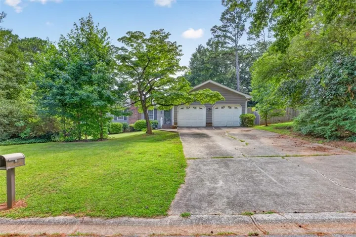 Ranch-style exterior with gray siding, a two-car garage, mature trees, a well-maintained lawn, and a concrete driveway
