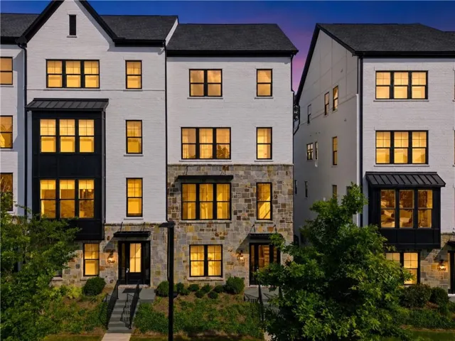 Modern townhome exterior with white brick facade, black-framed windows, stone accent detailing, and dark metal awnings