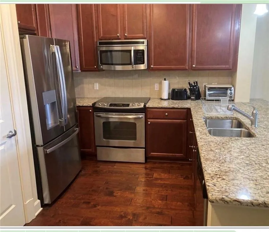 Kitchen featuring stainless steel appliances, light stone countertops, dark wood-type flooring, and tasteful backsplash