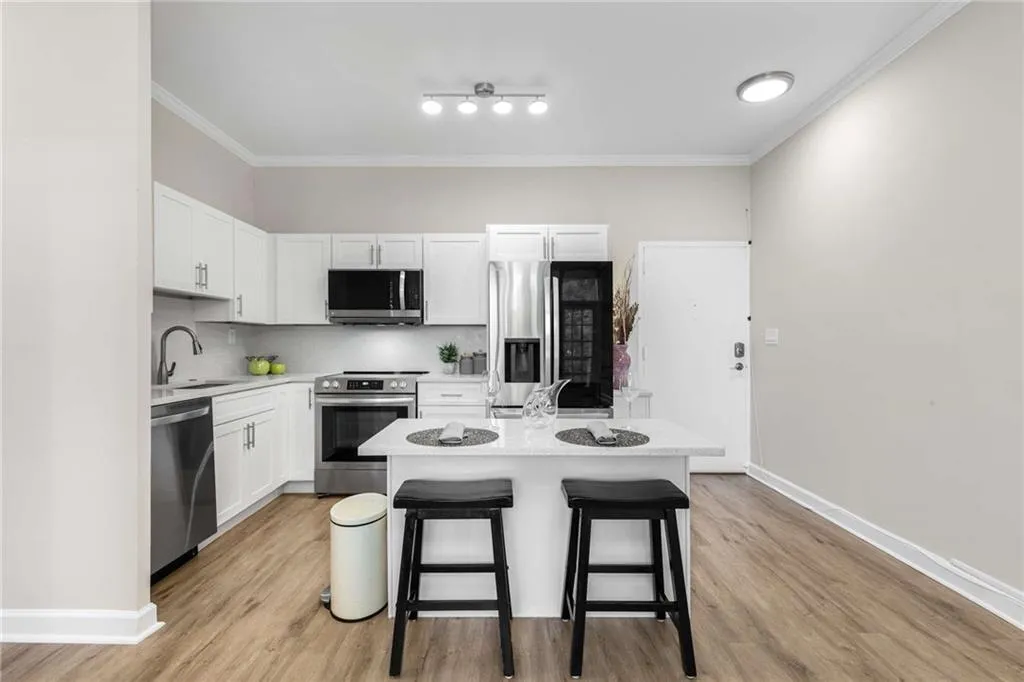 Kitchen with appliances with stainless steel finishes, ornamental molding, white cabinets, tasteful backsplash, and a breakfast bar area