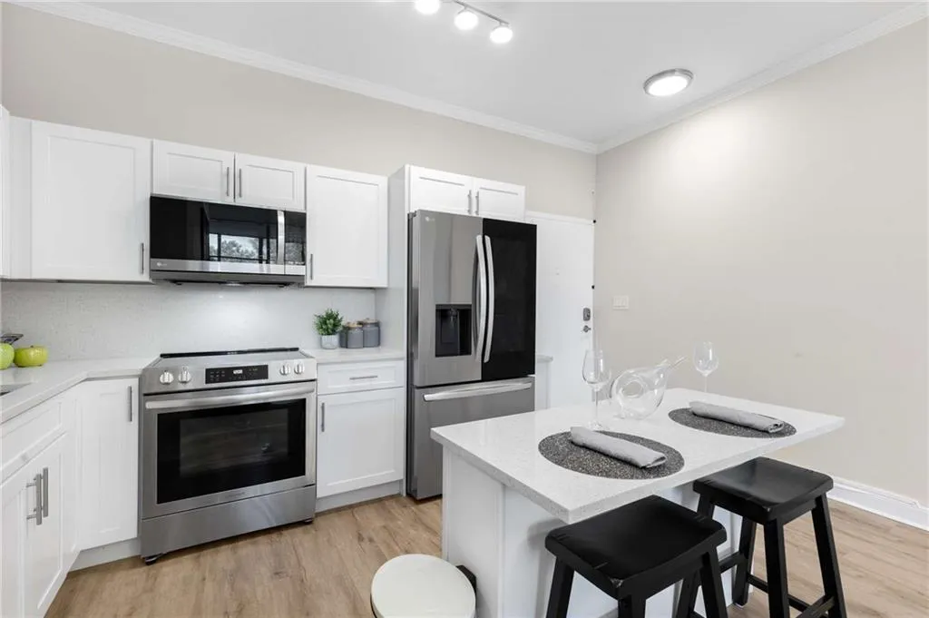 Kitchen with crown molding, stainless steel appliances, a kitchen breakfast bar, light wood finished floors, and white cabinetry
