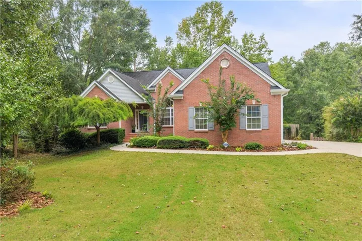 Brick exterior featuring a gabled roofline, decorative window shutters, and mature landscaping