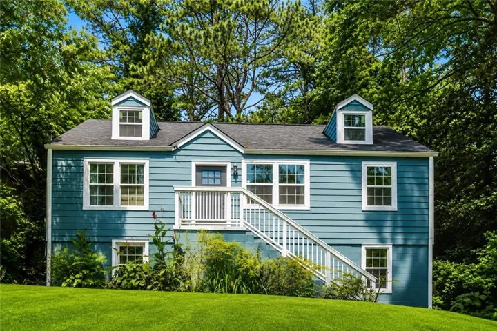 Turquoise blue siding exterior featuring white trim, a dark shingle roof, two dormer windows, and a prominent front entrance with a white railing and staircase