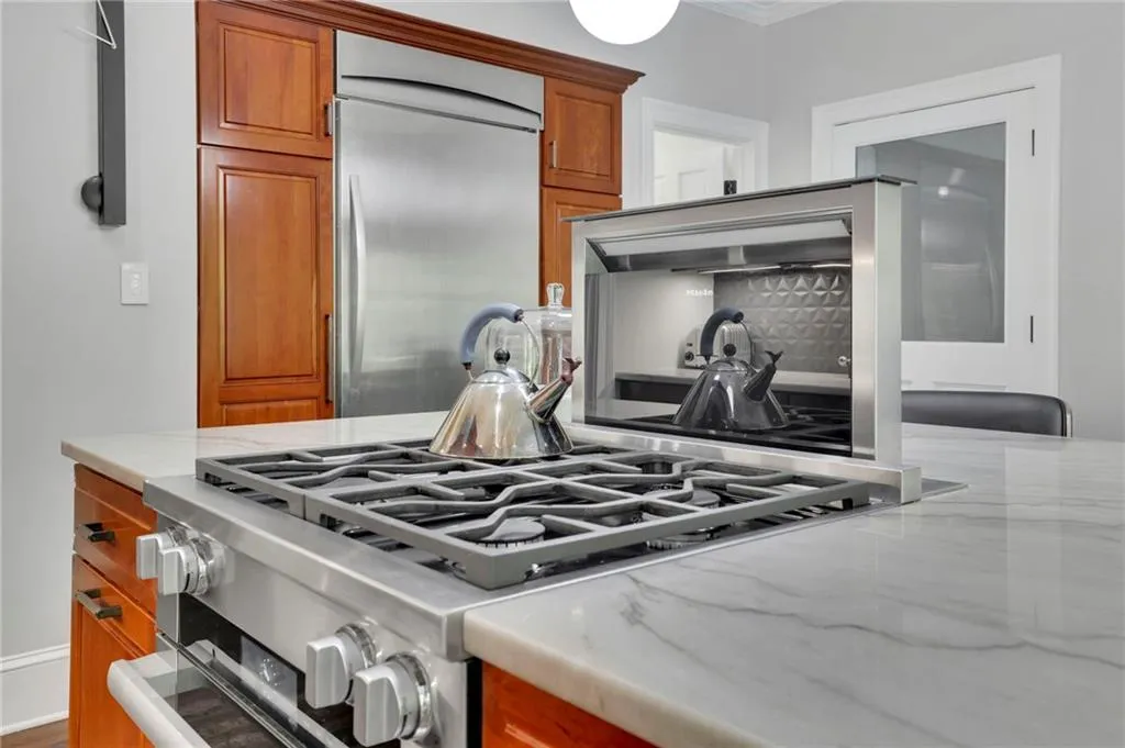 Kitchen with backsplash, stainless steel dishwasher, brown cabinets, light stone counters, and ornamental molding