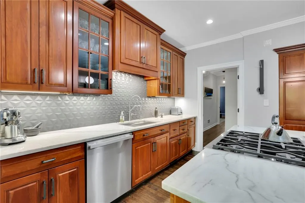 Kitchen featuring brown cabinetry, a kitchen breakfast bar, appliances with stainless steel finishes, decorative light fixtures, and dark wood-style floors