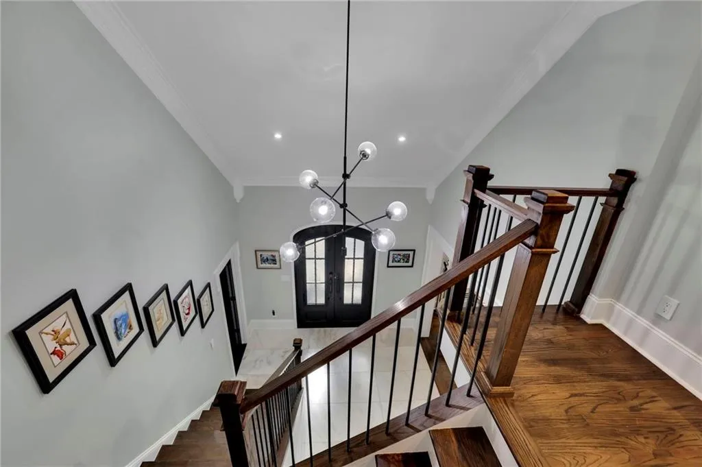 Stairway with ornamental molding, french doors, a chandelier, and wood finished floors