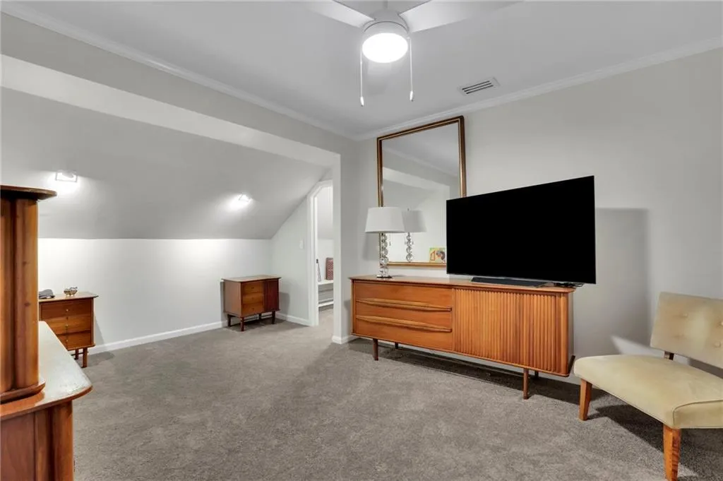 Living area with vaulted ceiling, light carpet, ornamental molding, and a ceiling fan