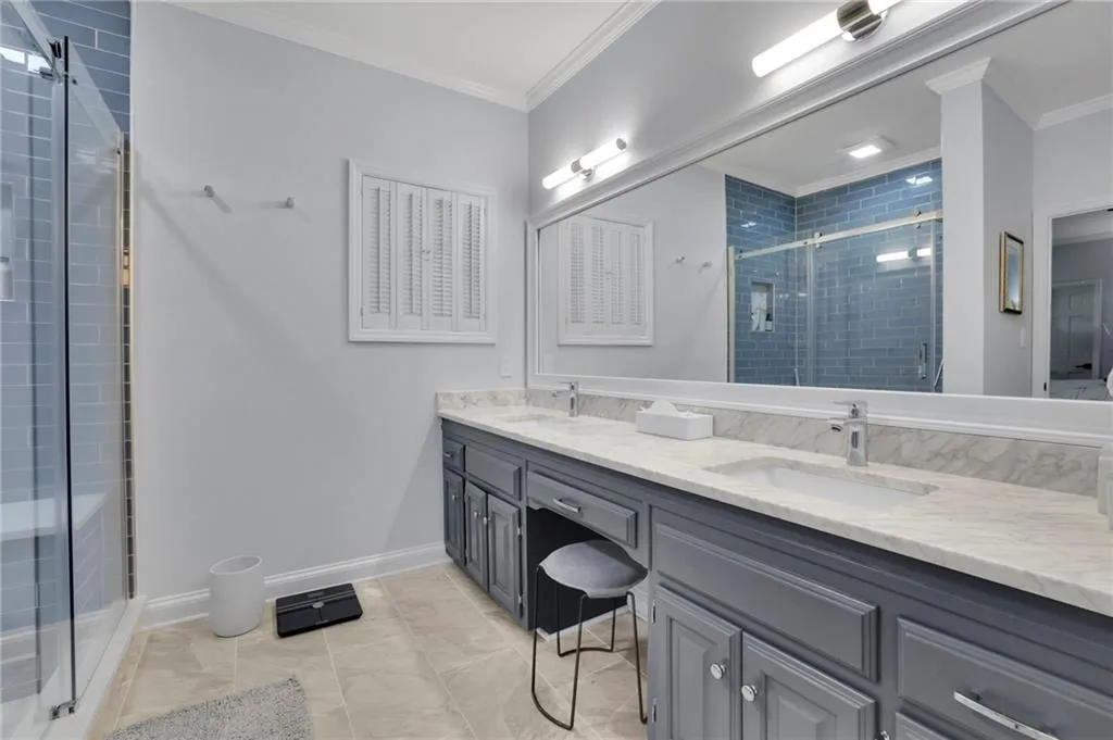 Bathroom with a shower stall, double vanity, ornamental molding, and light tile patterned floors