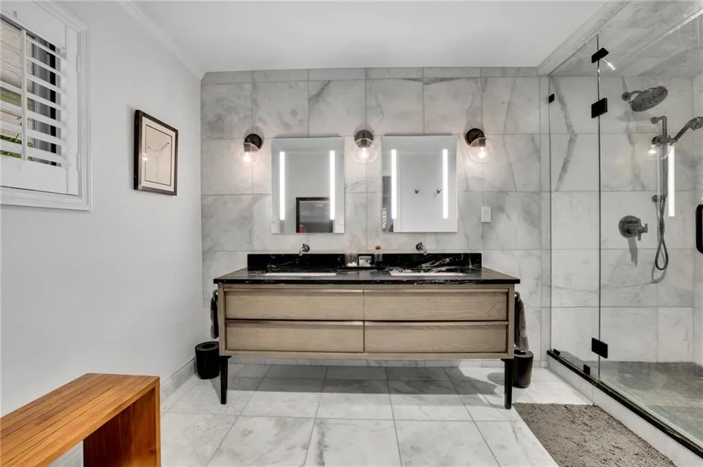 Full bath with a marble finish shower, double vanity, and tile walls