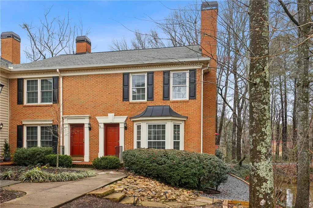 Colonial home with a chimney, brick siding, and a shingled roof
