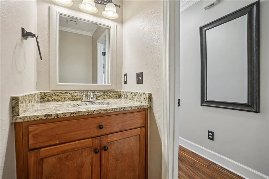 Bathroom featuring a textured wall, ornamental molding, vanity, and dark wood finished floors