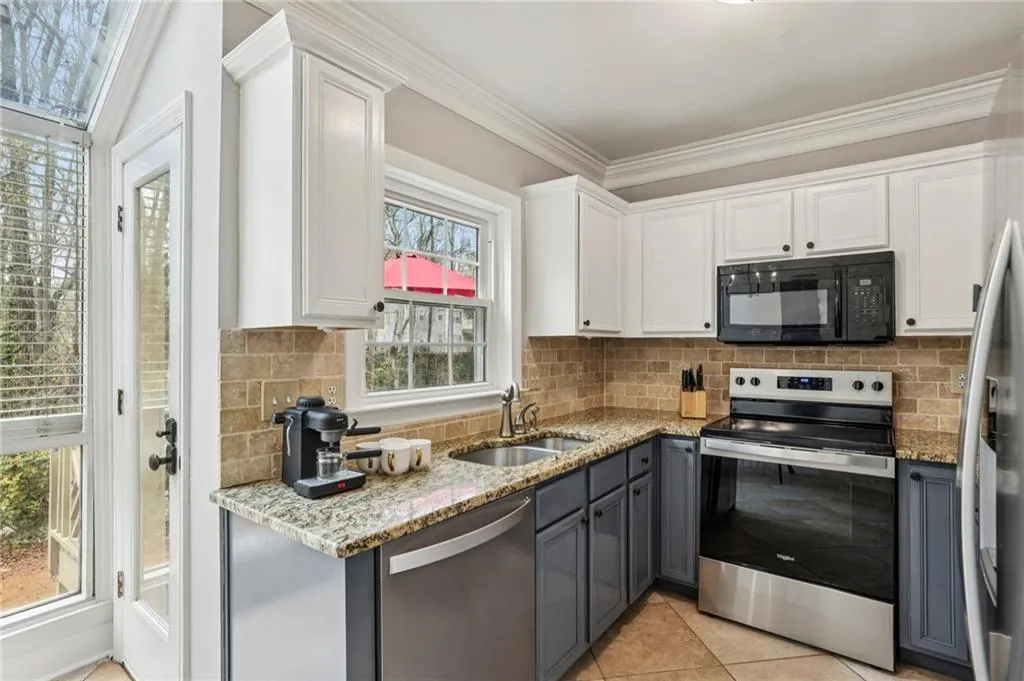 Kitchen with dual tone cabinetry, stainless steel appliances, light stone countertops, backsplash, and crown molding