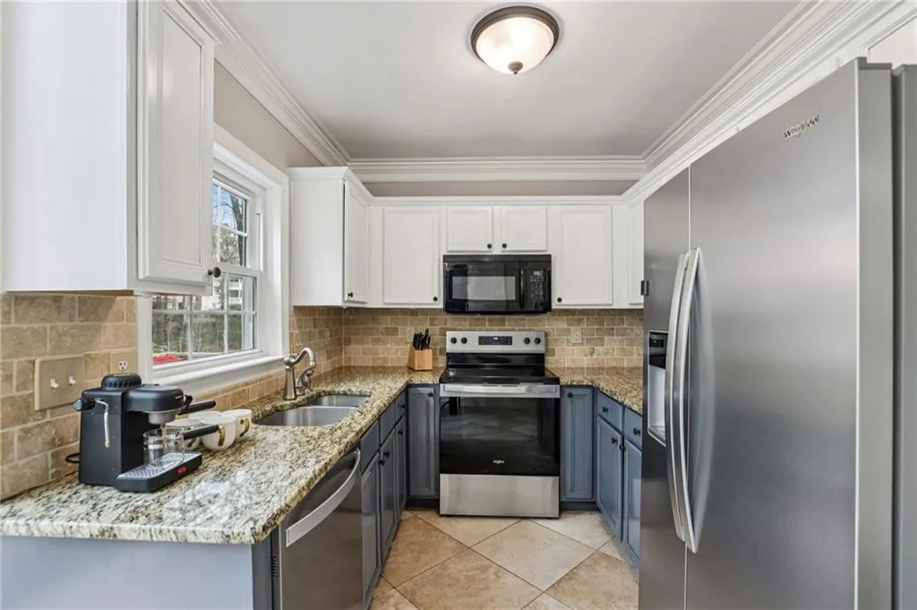 Two tone kitchen featuring light stone counters, two tone color scheme, stainless steel appliances, light tile patterned flooring, and ornamental molding