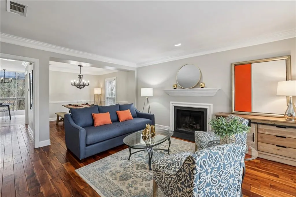Living room with a fireplace with flush hearth, dark wood-type flooring, ornamental molding, and suspended lighting