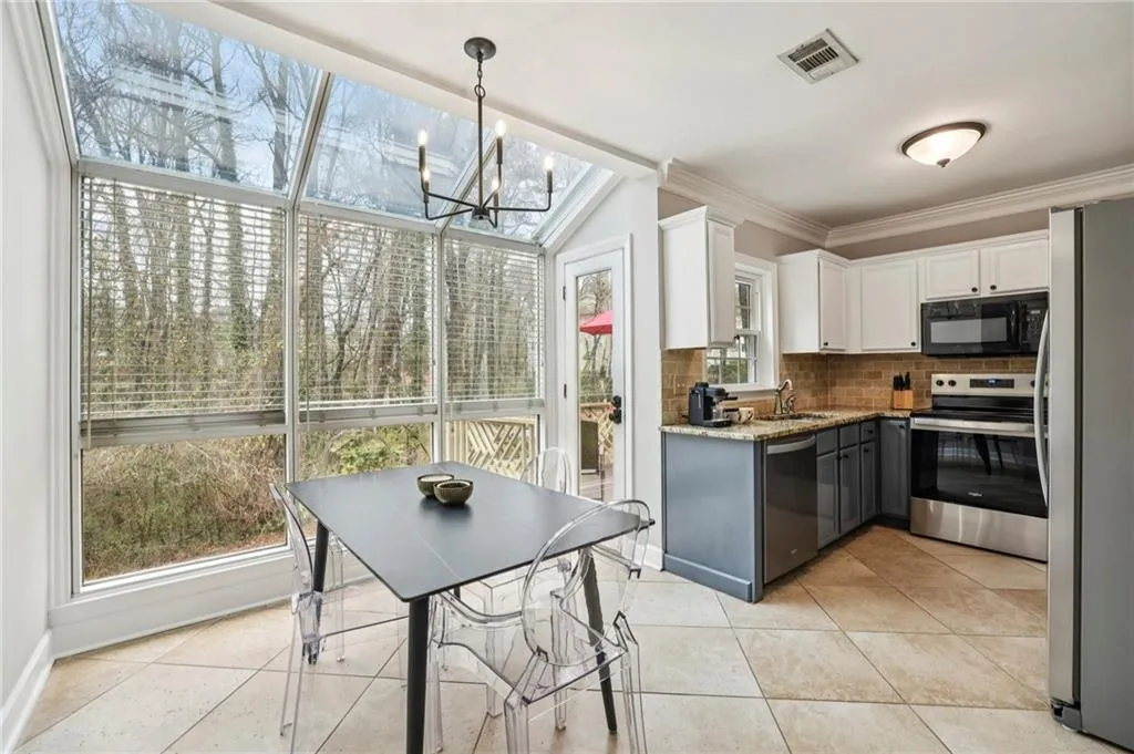Two tone kitchen featuring dual tone cabinetry, stainless steel appliances, light stone counters, decorative backsplash, and light tile patterned flooring