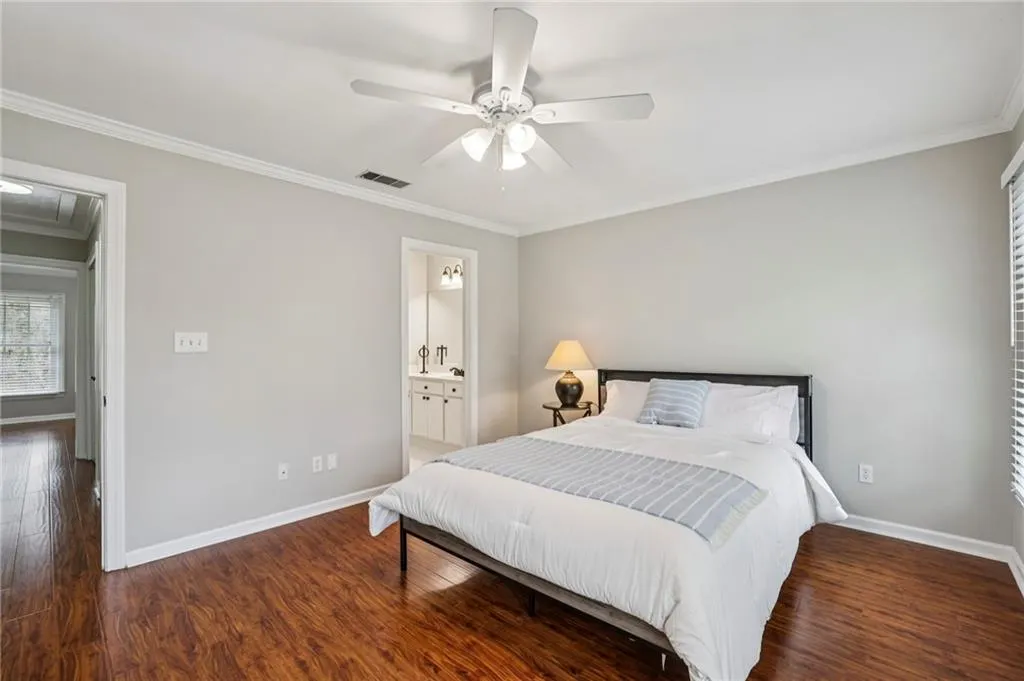 Bedroom featuring ornamental molding, dark wood-type flooring, a ceiling fan, and ensuite bathroom