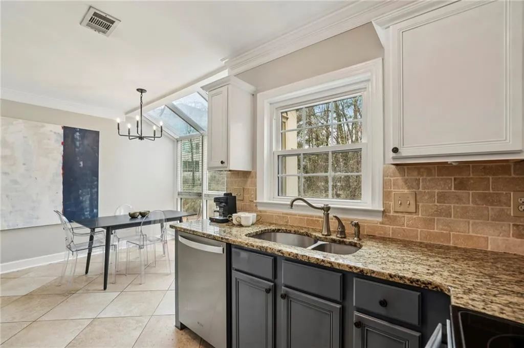 Kitchen featuring backsplash, dishwasher, crown molding, light stone countertops, and light tile patterned flooring