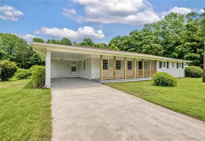 White brick exterior featuring a covered carport, full-length front porch with wood railings, and a concrete driveway