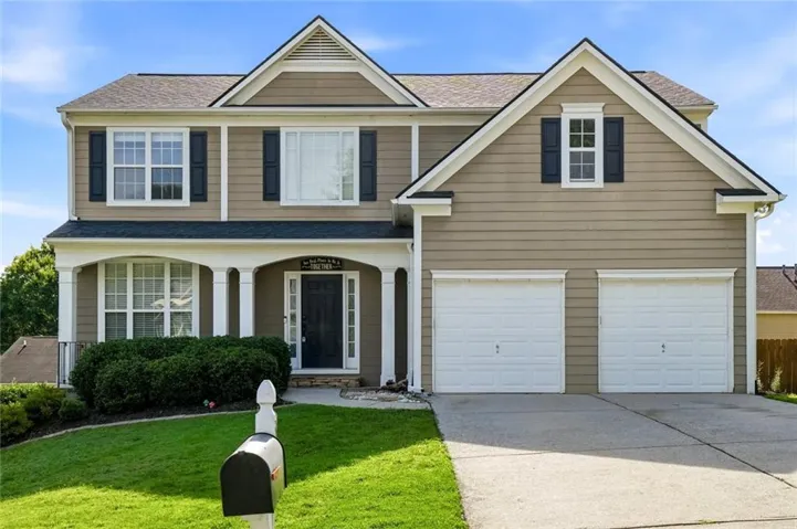 Two-story property featuring a neutral-toned siding exterior, a covered front porch with white columns, a two-car garage with white doors, a concrete driveway, and a manicured front lawn