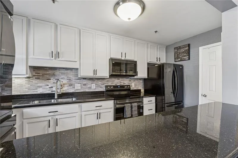 Kitchen featuring white cabinetry, dark stone counters, stainless steel appliances, and backsplash