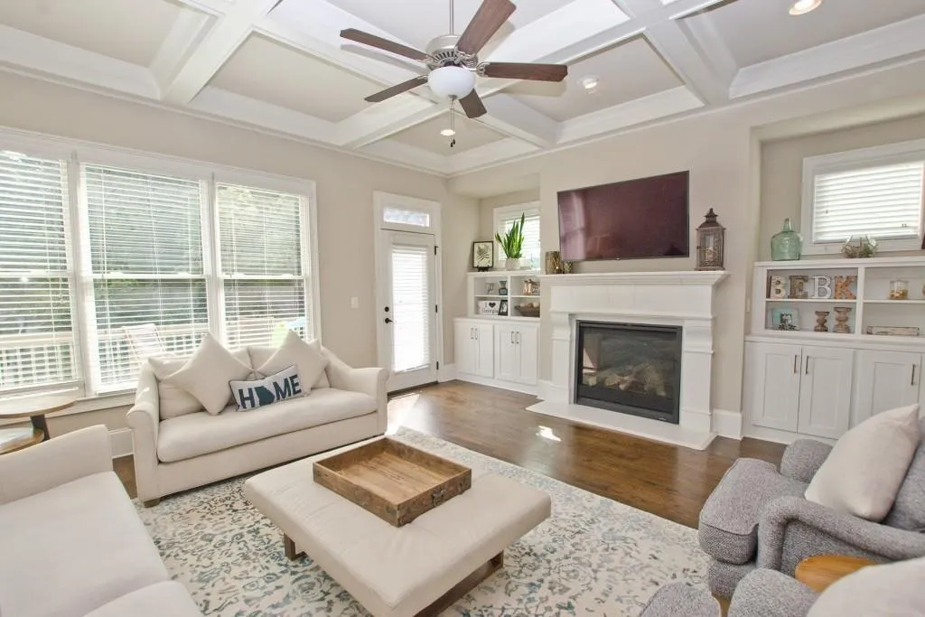 Living area featuring coffered ceiling, ceiling fan, a glass covered fireplace, wood finished floors, and beam ceiling