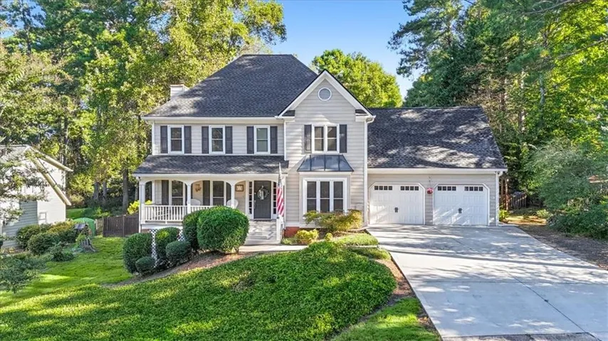 Two-story residence featuring light gray siding, dark shutters, a covered front porch, and an attached two-car garage