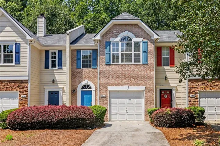 Exterior featuring brick and siding finishes, individual garage, arched entryway, and mature landscaping