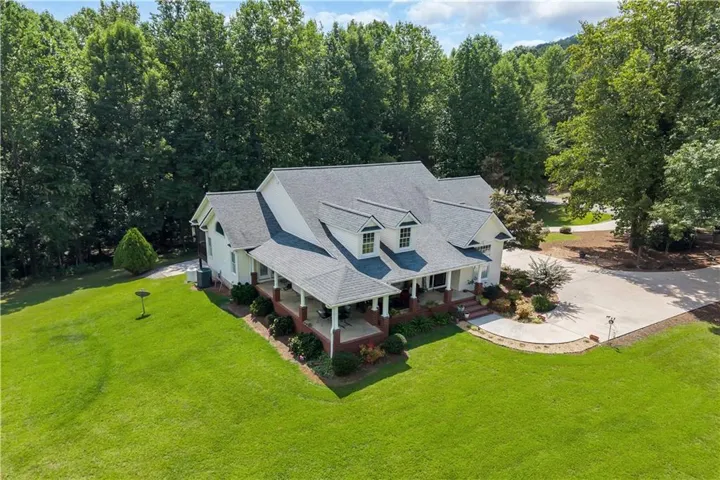 Manicured lawn surrounding a residence with a covered front porch, dormer windows, attached garage, and a concrete driveway