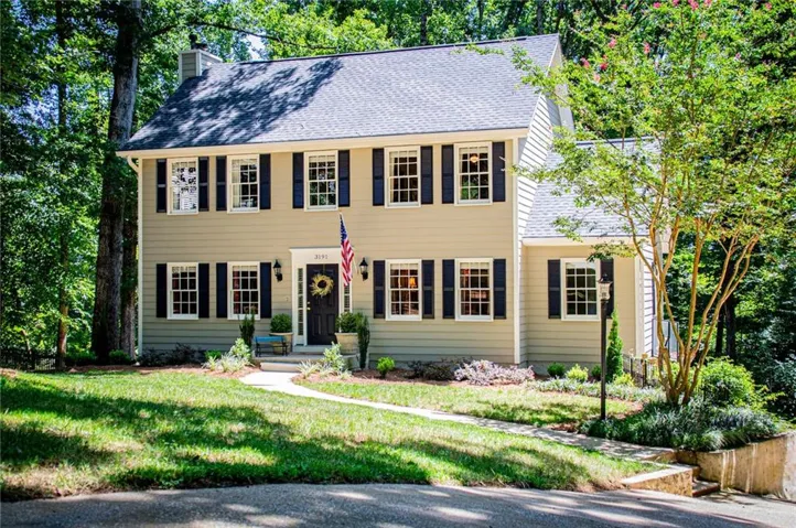 Classic Colonial-style residence featuring a cream exterior with black shutters and trim, symmetrical facade with multiple multi-pane windows, slate-gray pitched roof, and a covered front entrance with classical detailing