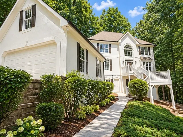 Stucco exterior with dark-toned shutters, a multi-pane arched window, an elevated front deck, and an attached garage with a panel door